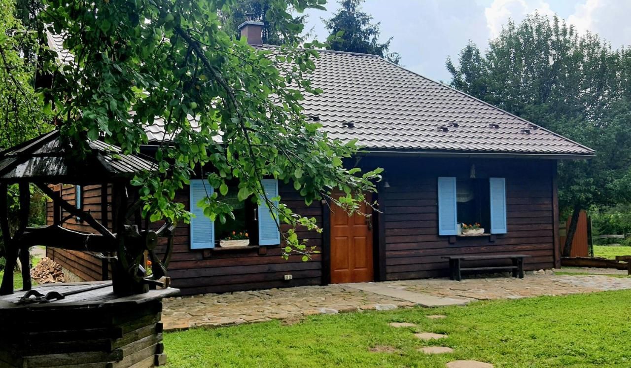 Przed domem kamienny taras, ława pod oknem i drewniana studnia pod gałęziami drzewa